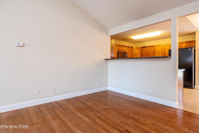 kitchen with a textured ceiling, light wood-type flooring, and fridge