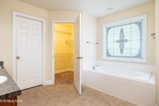 bathroom featuring tile patterned flooring, vanity, and a relaxing tiled tub