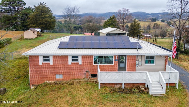 rear view of property with solar panels, a shed, a deck, and a lawn