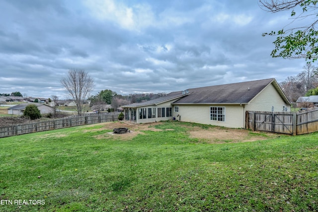 rear view of property with a sunroom, a yard, and an outdoor fire pit