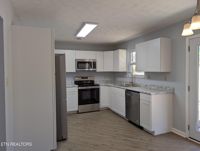 kitchen featuring a textured ceiling, stainless steel appliances, decorative light fixtures, light hardwood / wood-style flooring, and white cabinets