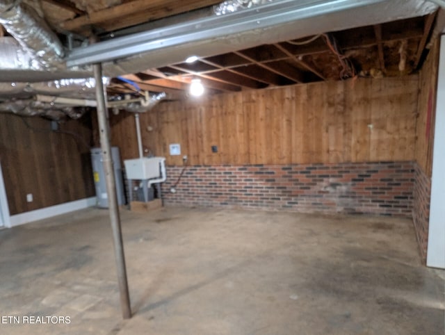 basement featuring wood walls, gas water heater, and brick wall