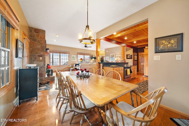 dining space featuring wooden ceiling, ceiling fan with notable chandelier, beam ceiling, a fireplace, and light hardwood / wood-style floors