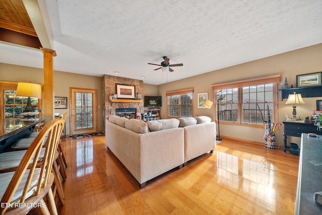 living room featuring a fireplace, a textured ceiling, light hardwood / wood-style flooring, and ceiling fan