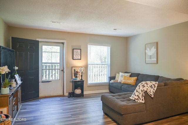 living room with a wealth of natural light, dark wood-type flooring, and a textured ceiling