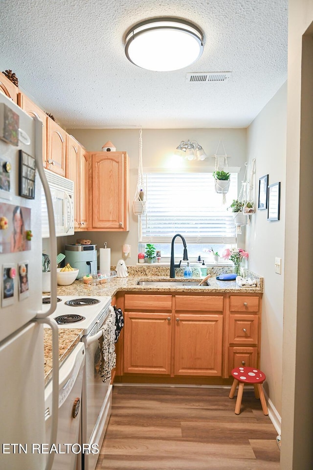 kitchen with light stone countertops, white appliances, a textured ceiling, hardwood / wood-style floors, and sink