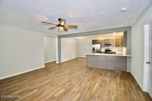 kitchen with a textured ceiling, kitchen peninsula, light wood-type flooring, and stainless steel appliances