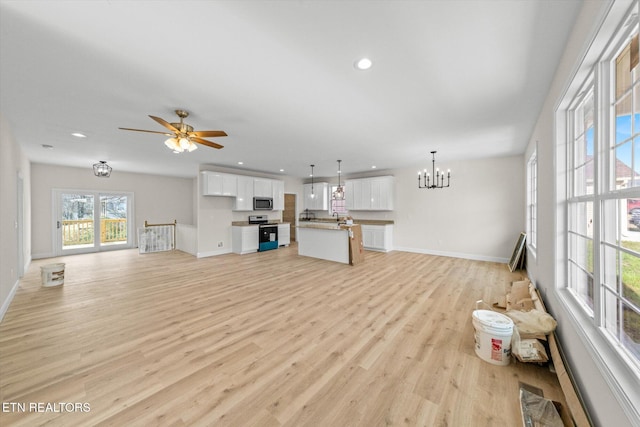 unfurnished living room featuring ceiling fan with notable chandelier and light hardwood / wood-style flooring