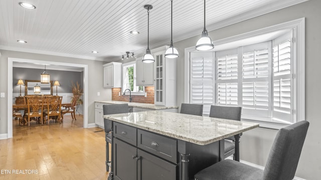 kitchen with a kitchen bar, light wood-type flooring, decorative light fixtures, a center island, and white cabinetry