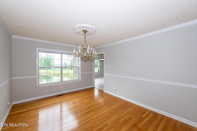 empty room with a chandelier, wood finished floors, a textured ceiling, baseboards, and ornamental molding