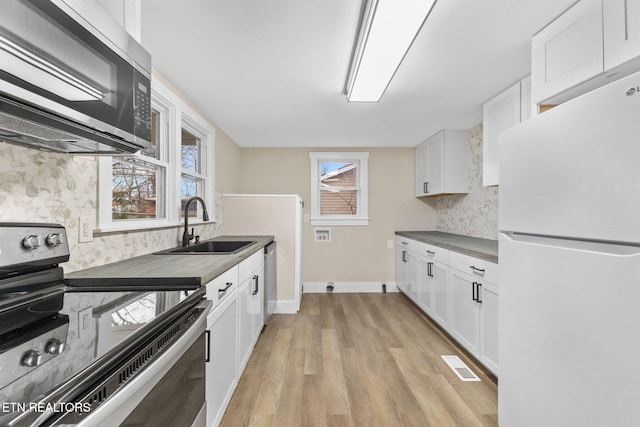 kitchen featuring sink, tasteful backsplash, appliances with stainless steel finishes, white cabinets, and light wood-type flooring