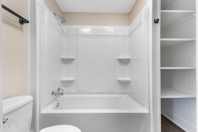 bathroom with shower / bathing tub combination, toilet, and a textured ceiling