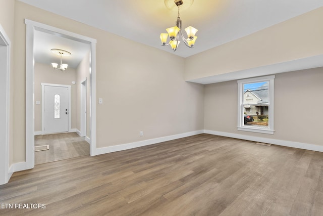 spare room with wood-type flooring, an inviting chandelier, and a wealth of natural light