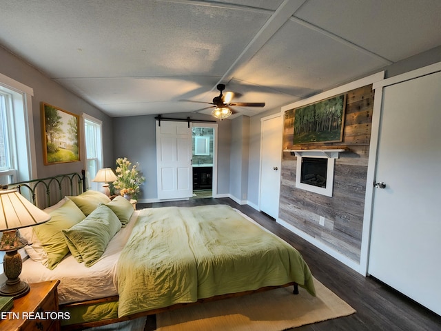 bedroom featuring ensuite bath, vaulted ceiling, dark wood-type flooring, and a barn door