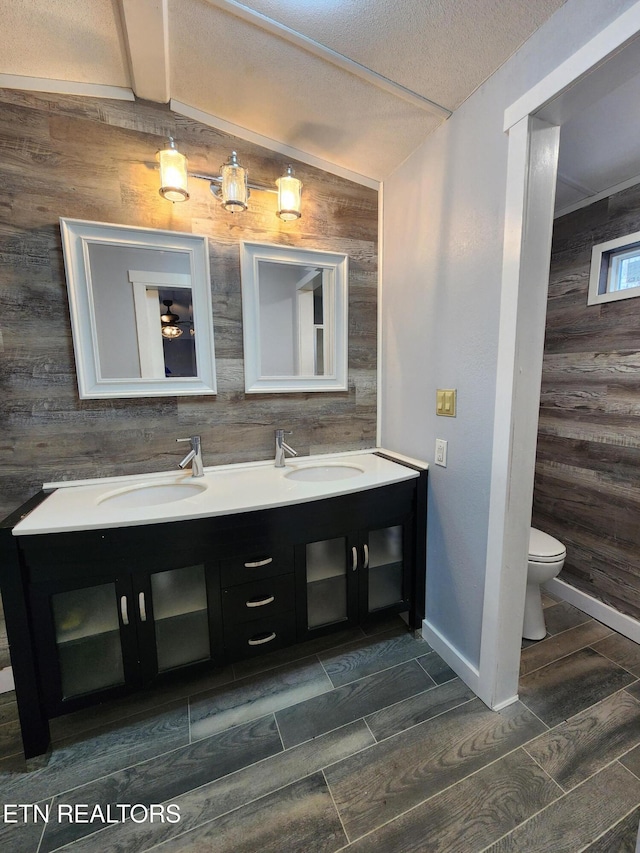 bathroom featuring vanity, toilet, a textured ceiling, and wooden walls