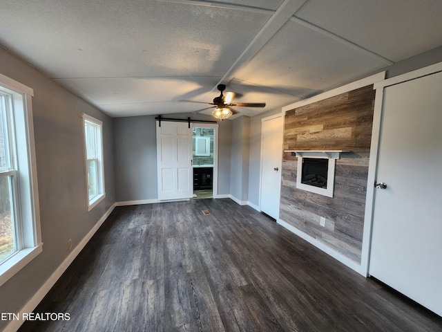 unfurnished living room featuring vaulted ceiling, a textured ceiling, ceiling fan, dark hardwood / wood-style flooring, and a barn door