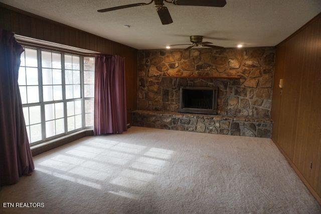 unfurnished living room with a stone fireplace, wood walls, light colored carpet, and a textured ceiling