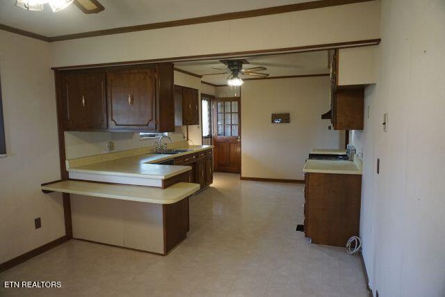 kitchen featuring kitchen peninsula, dark brown cabinetry, ceiling fan, crown molding, and sink