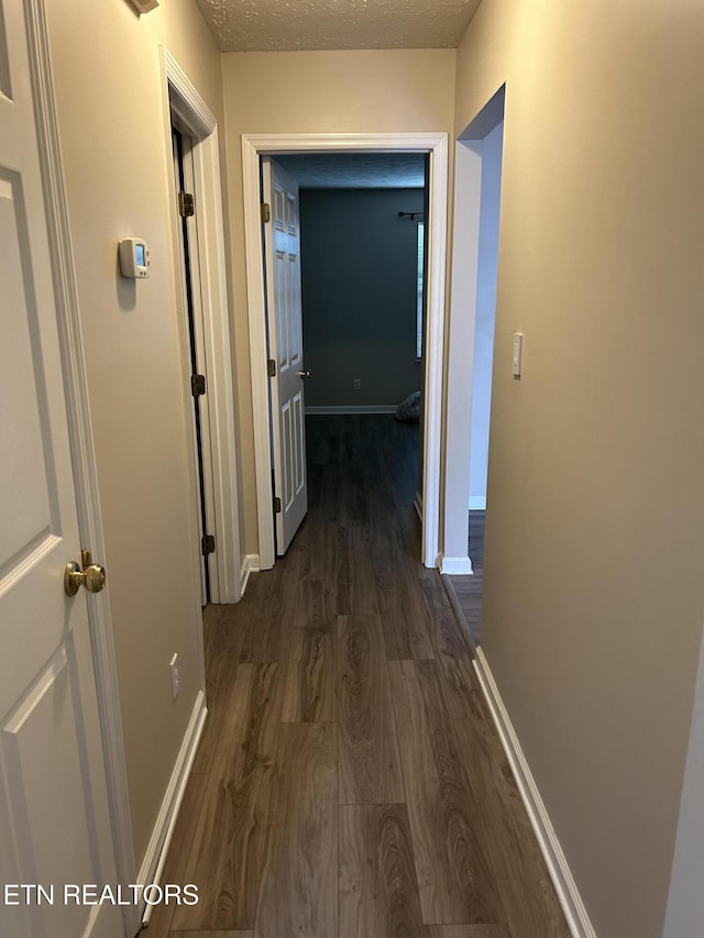 corridor featuring a textured ceiling and dark hardwood / wood-style flooring