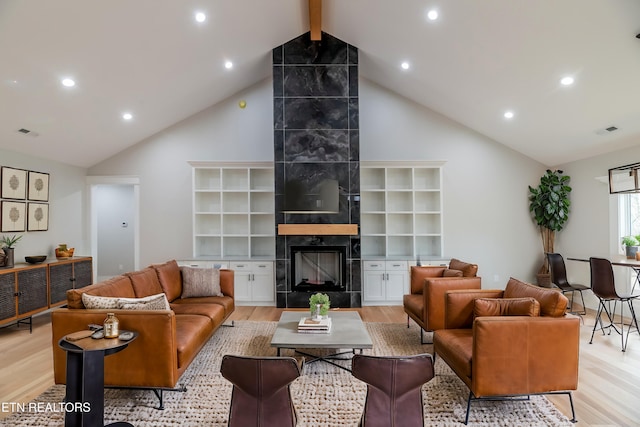 living area featuring visible vents, light wood-type flooring, beam ceiling, a tile fireplace, and high vaulted ceiling