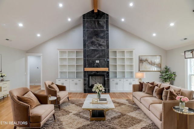 living area featuring visible vents, light wood finished floors, high vaulted ceiling, a fireplace, and beamed ceiling