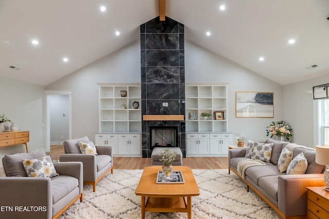 living room featuring visible vents, a tiled fireplace, light wood-type flooring, beam ceiling, and high vaulted ceiling