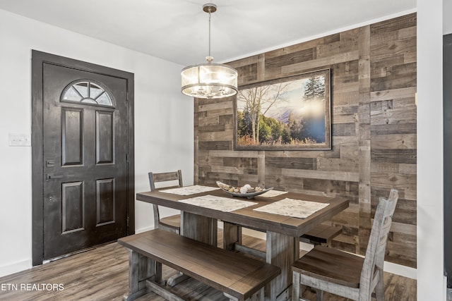 dining space featuring hardwood / wood-style flooring, wooden walls, and a chandelier