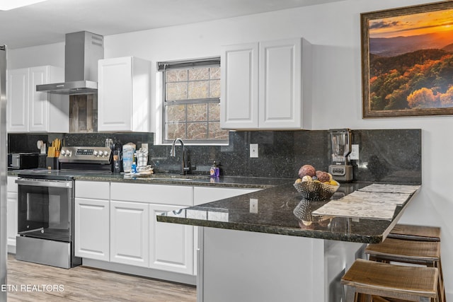 kitchen featuring stainless steel electric range oven, light hardwood / wood-style flooring, white cabinets, and wall chimney range hood