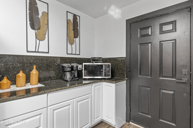 kitchen featuring light wood-type flooring, white cabinetry, backsplash, and dark stone counters