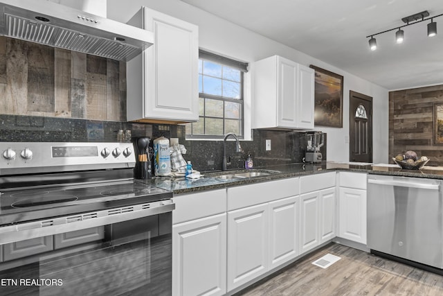 kitchen featuring white cabinets, decorative backsplash, stainless steel appliances, and wall chimney exhaust hood