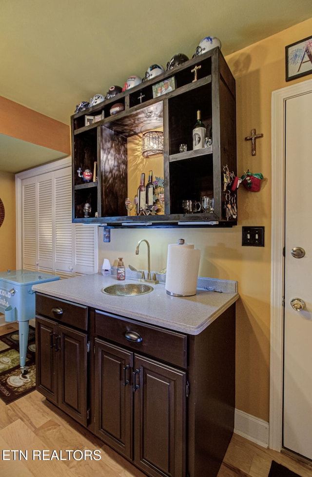 bar featuring dark brown cabinetry, sink, and light hardwood / wood-style flooring