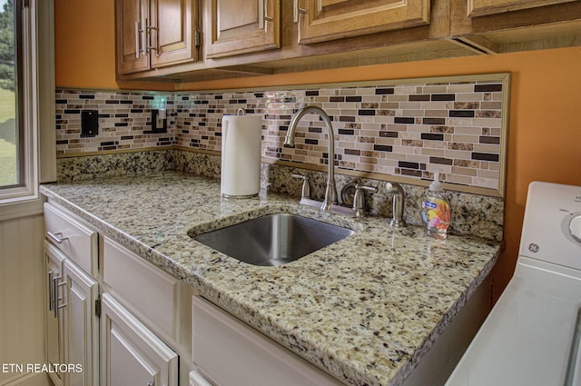 kitchen with light stone countertops, washer / dryer, decorative backsplash, and sink