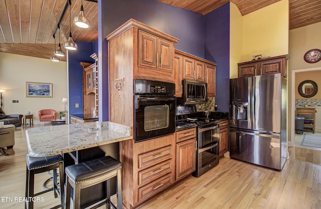 kitchen featuring dark stone counters, a breakfast bar area, light wood-type flooring, wood ceiling, and stainless steel appliances