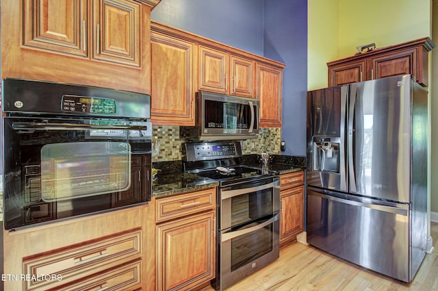 kitchen featuring appliances with stainless steel finishes, light wood-type flooring, tasteful backsplash, and dark stone counters