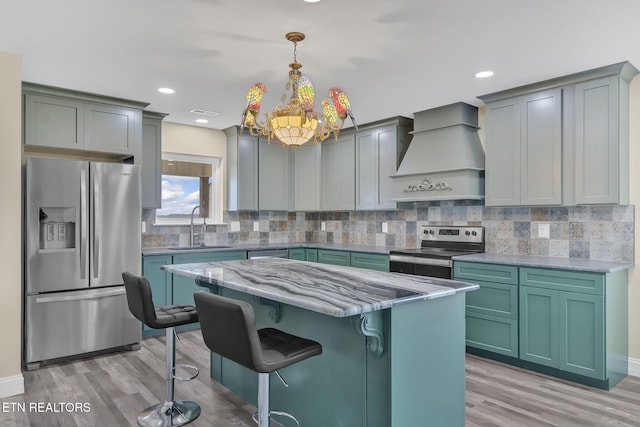 kitchen with a kitchen bar, appliances with stainless steel finishes, custom range hood, sink, and pendant lighting