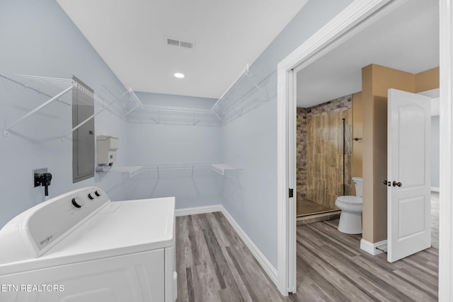 clothes washing area with electric panel, washer / clothes dryer, and light hardwood / wood-style flooring