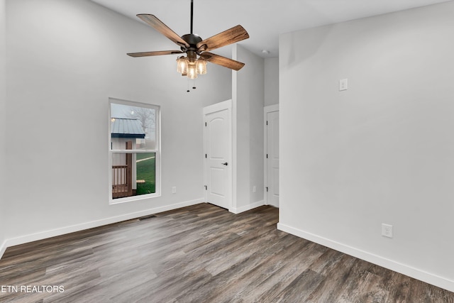 empty room featuring ceiling fan, a towering ceiling, and dark wood-type flooring