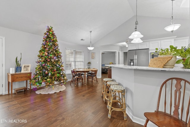 kitchen featuring white cabinetry, dark hardwood / wood-style floors, stainless steel refrigerator with ice dispenser, pendant lighting, and vaulted ceiling