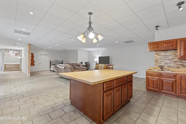 kitchen with pendant lighting, a drop ceiling, a center island, sink, and tasteful backsplash