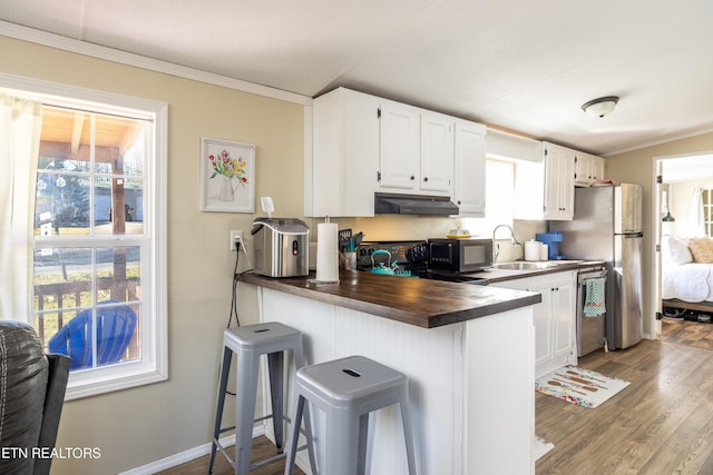 kitchen with kitchen peninsula, appliances with stainless steel finishes, wood-type flooring, white cabinets, and a breakfast bar area