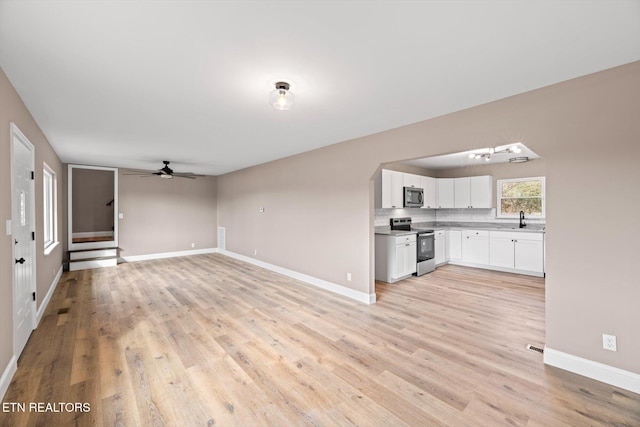 unfurnished living room featuring light wood-type flooring, ceiling fan, and sink