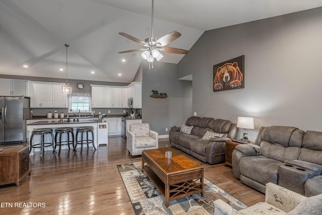 living room featuring ceiling fan, light hardwood / wood-style floors, sink, and vaulted ceiling