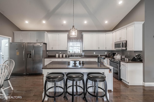 kitchen with appliances with stainless steel finishes, a center island, white cabinetry, and vaulted ceiling