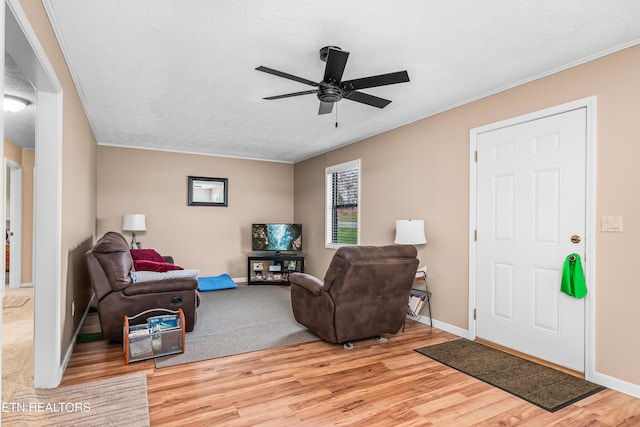 living room featuring ceiling fan, light hardwood / wood-style flooring, a textured ceiling, and ornamental molding