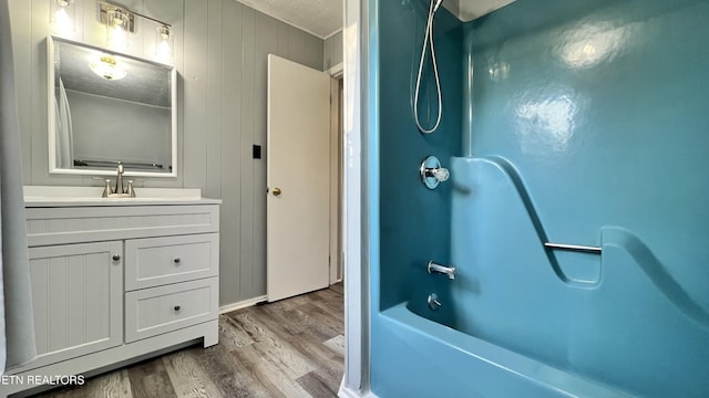 bathroom with wood-type flooring, a textured ceiling, wooden walls, vanity, and bathtub / shower combination