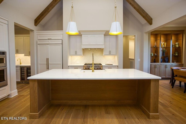 kitchen with vaulted ceiling with beams, a kitchen island with sink, hanging light fixtures, and tasteful backsplash