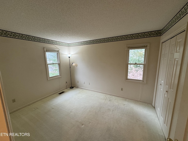 unfurnished bedroom with light colored carpet, a closet, and a textured ceiling