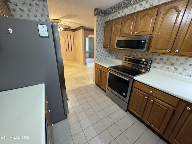 kitchen with ceiling fan, stainless steel appliances, a textured ceiling, and light tile patterned floors