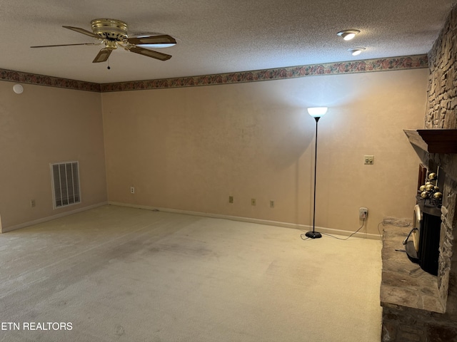 basement with ceiling fan, a stone fireplace, light carpet, and a textured ceiling