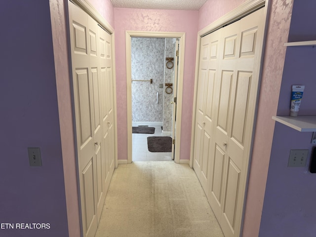 hallway with light carpet and a textured ceiling